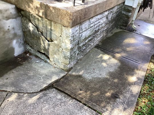 Damaged stone foundation and concrete steps of a building's entrance. The concrete is cracked and stained, while the foundation has large cracks.