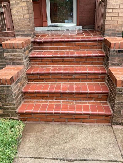 Brick steps leading up to a door, with brick detailing on the sides. Red brick is the primary color, with a concrete landing at the bottom.