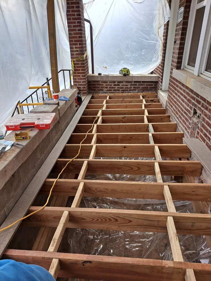 Wooden staircase under construction, framed with exposed joists. Construction materials and tools are visible on steps and to the side.