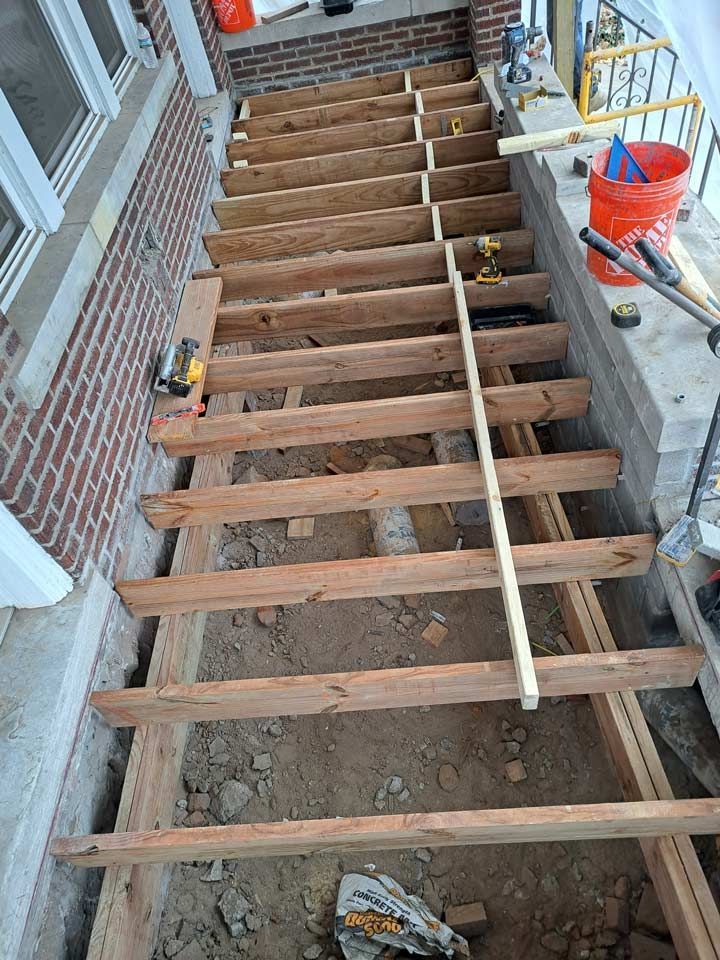 Wooden stair structure under construction.  Unfinished steps of wooden planks, with tools and materials visible on the side, outdoors.