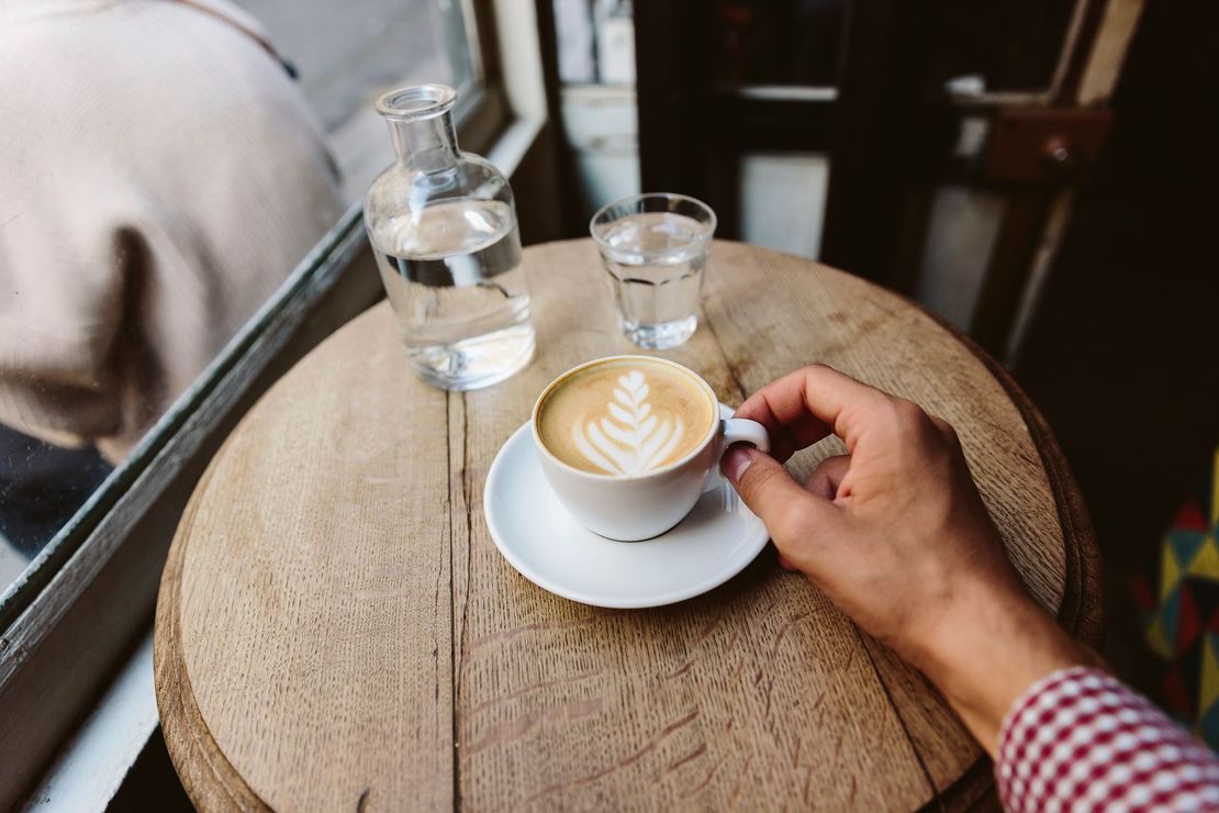 Una persona è seduta a un tavolo con una tazza di caffè e un bicchiere d'acqua.