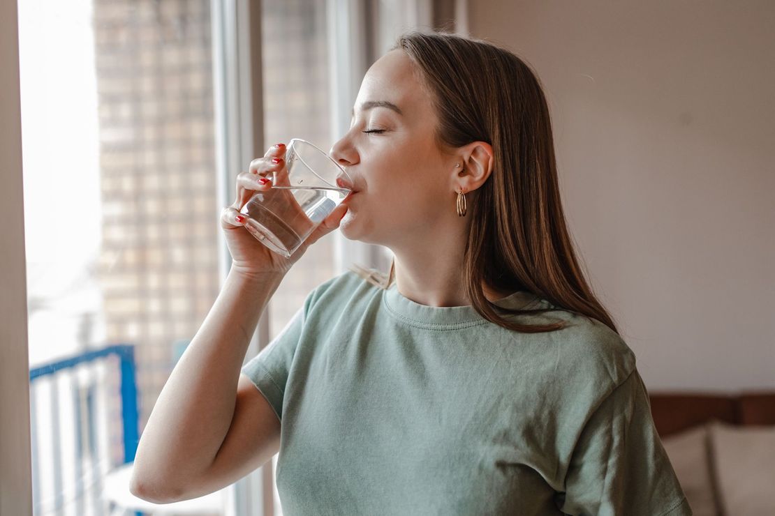 Una donna sta bevendo acqua da un bicchiere davanti a una finestra.