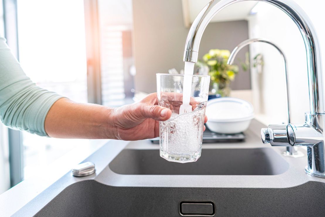 Una persona versa acqua in un bicchiere dal lavandino della cucina.