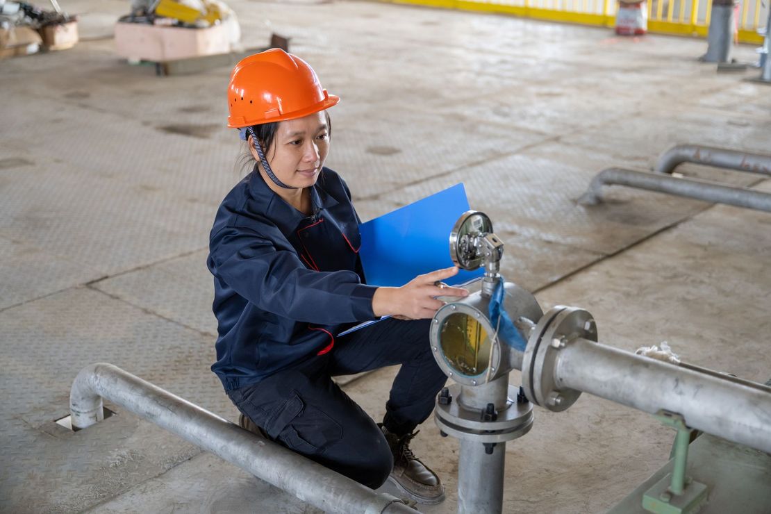Una donna con un casco sta lavorando su un tubo in una fabbrica.