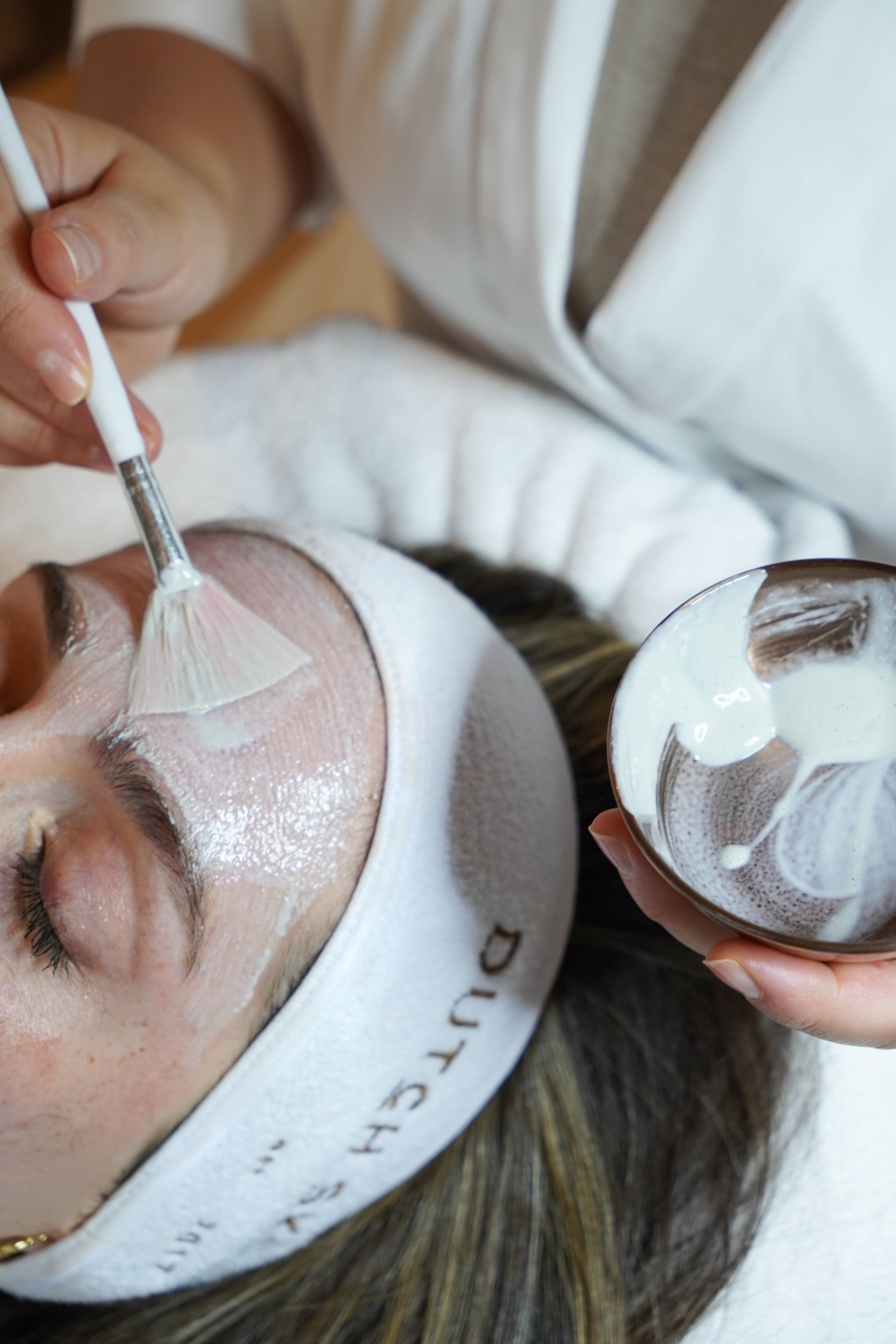 Een gezichtsmasker wordt met een kwast op het gezicht van een klant aangebracht tijdens behandeling.