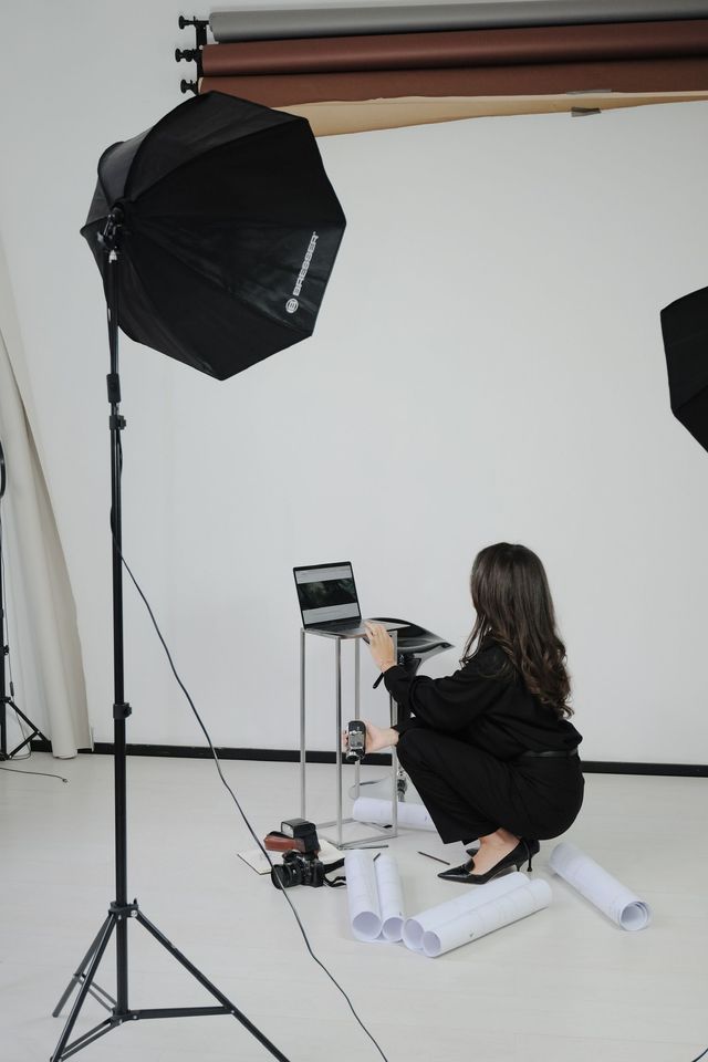 Een persoon knielt in een fotostudio naast een camerastatief en een grote softbox.