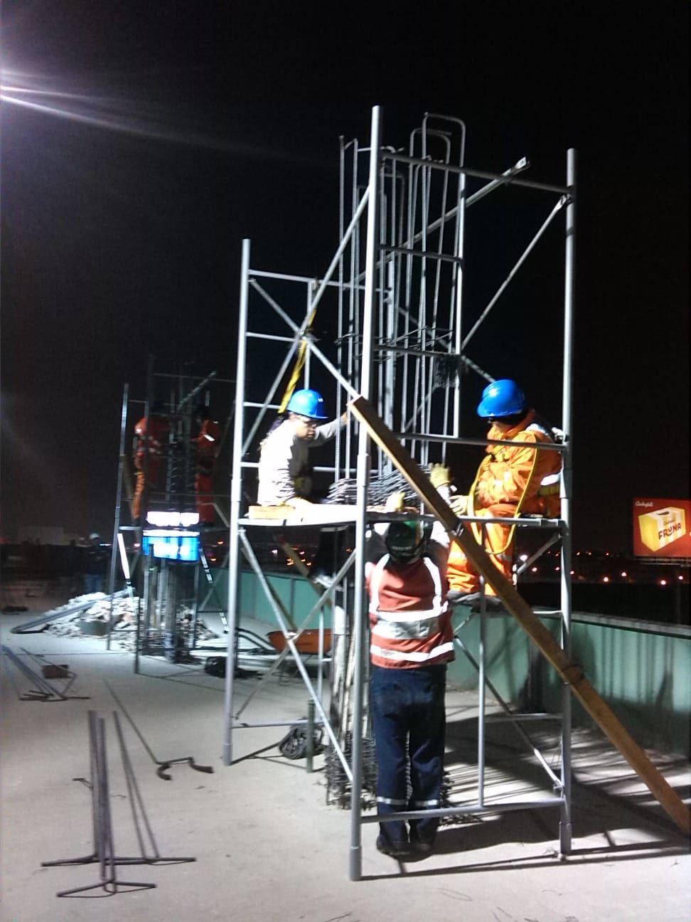 Un grupo de trabajadores de la construcción de pie sobre un andamio por la noche.