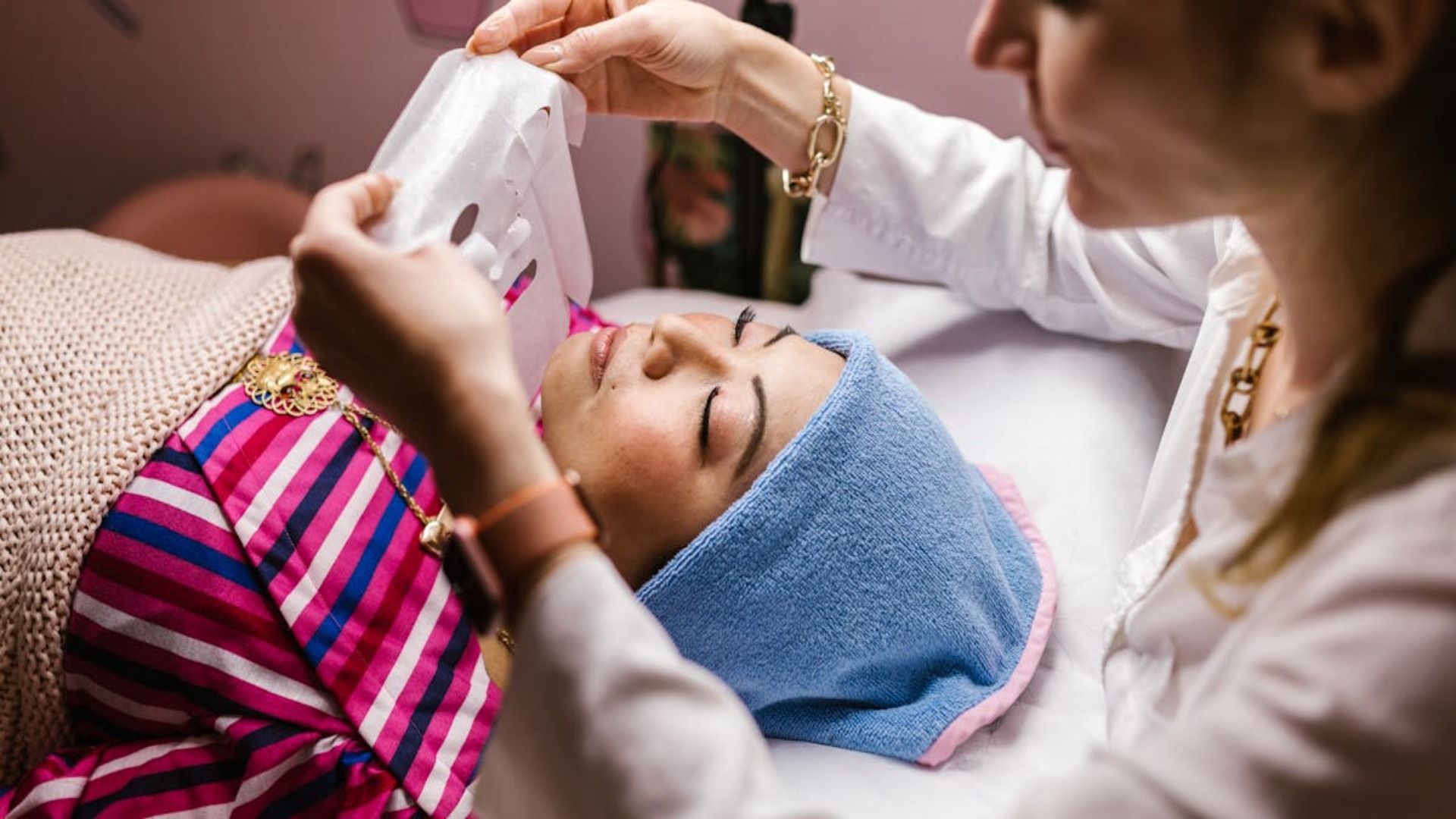 Una mujer le está dando a otra mujer un tratamiento facial con una toalla envuelta alrededor de su cabeza.