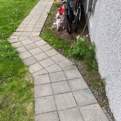 Steypt stígur sveigir í gegnum grasið við hliðina á byggingu. Reiðhjól og barnshjól eru lögð.