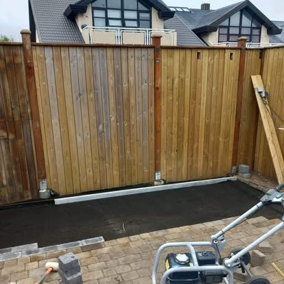 Trégirðing með rennihliði, við hliðina á malbikaðri lóð með þjöppu.