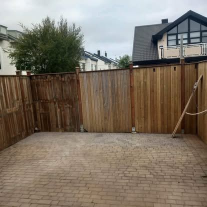 Trégirðing umlykur múrsteinsverönd. Hús í bakgrunni undir skýjuðum himni.