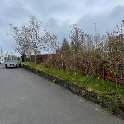 Götumynd með vörubíl, trjám, brúnni girðingu og grasi vaxinni bakka undir skýjuðum himni.