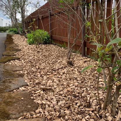 Garðbeð með mold við steinstíg og trégirðingu.