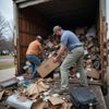 Two men unloading a truck filled with trash and boxes in a residential setting.