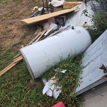 A pile of discarded junk outdoors, including a water heater, wood, and a door.