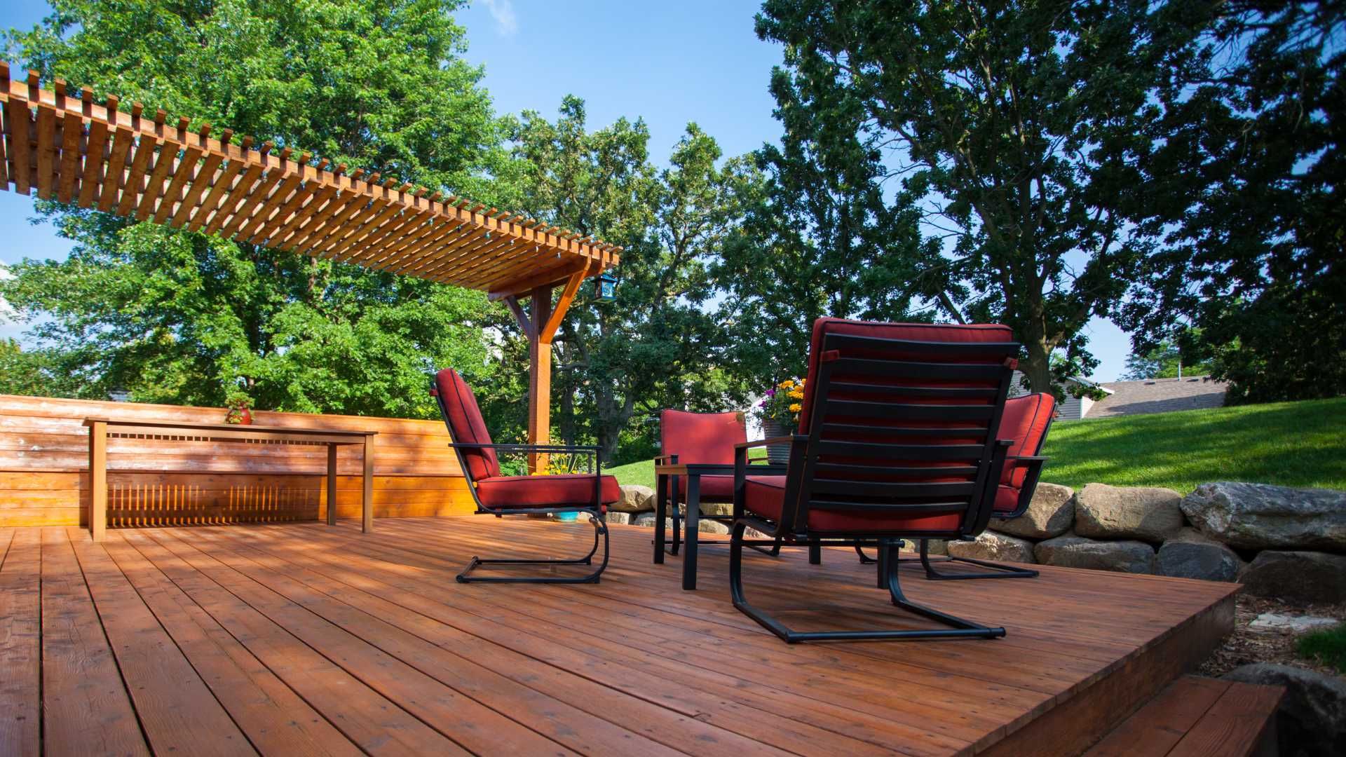 A wooden deck with chairs and a table under a pergola.