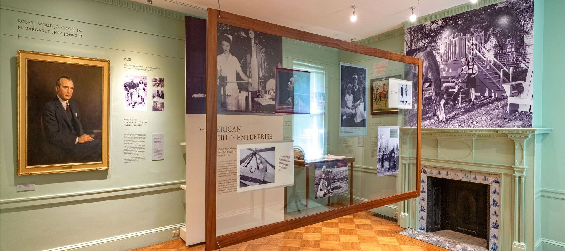 Museum exhibit with portrait, photos, and large wooden frame. Green and white walls, wood floor.