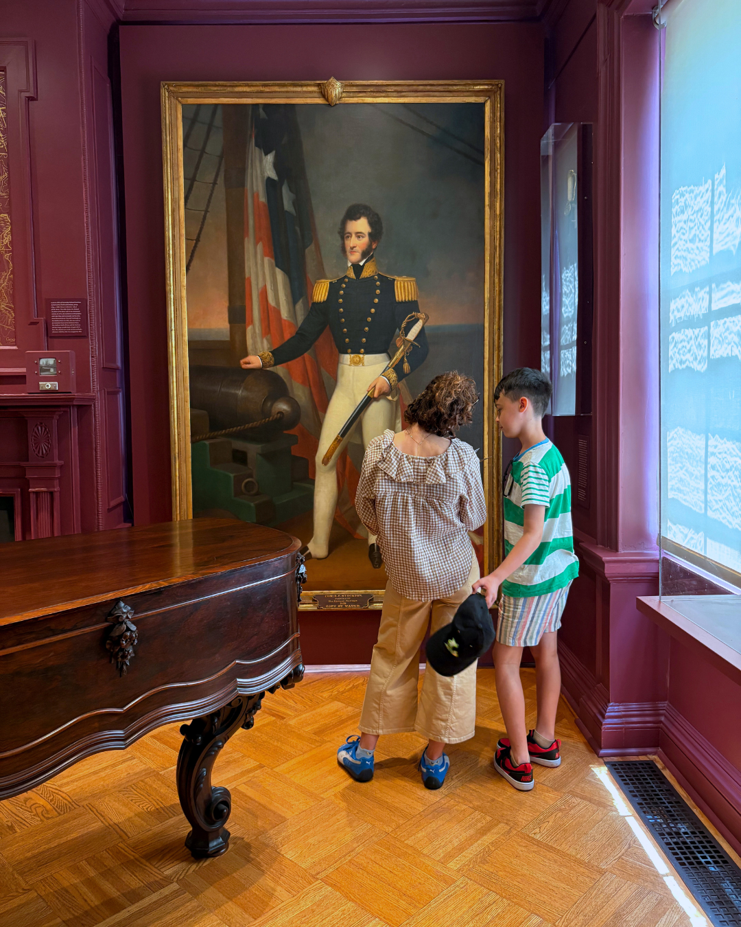 Two people look at a portrait in a gallery with red walls.