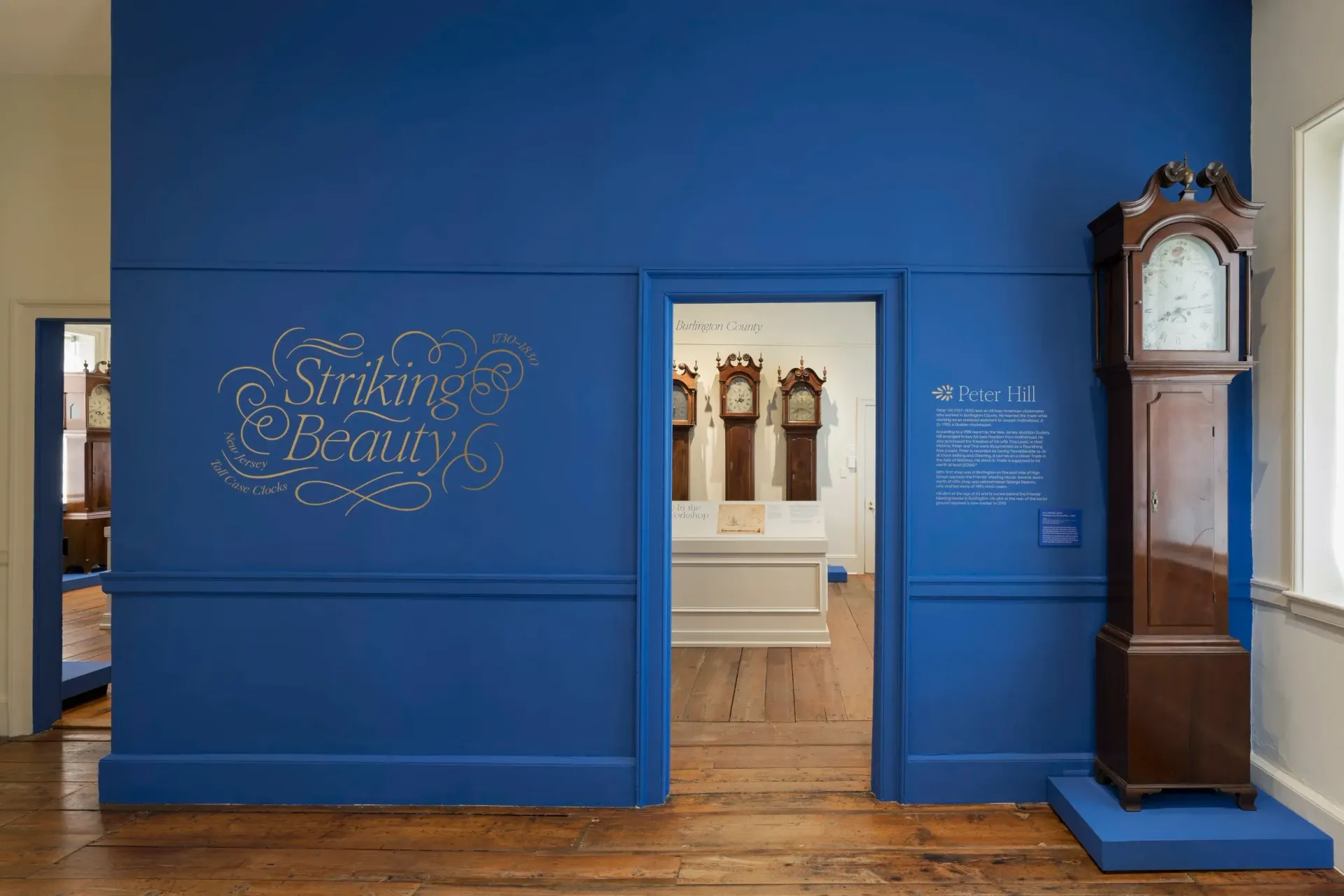 Blue-walled museum room with grandfather clock. Entrance to a room with more clocks.