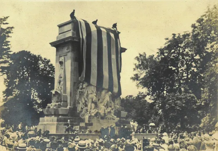 Monument unveiling, draped with striped fabric; crowd gathered outdoors.