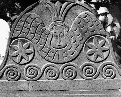 Stone carving of an angel with outstretched wings, flanked by stars, atop a tombstone.
