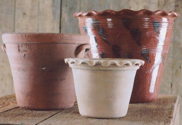 Three terracotta flower pots, varying sizes, on a wooden surface. One has a fluted rim.