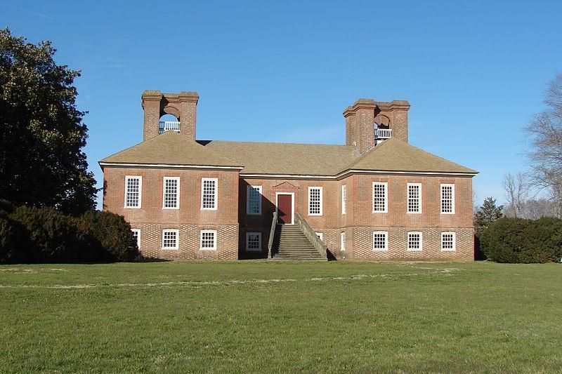 A large, light-colored mansion surrounded by greenery with a grand staircase and lawn.