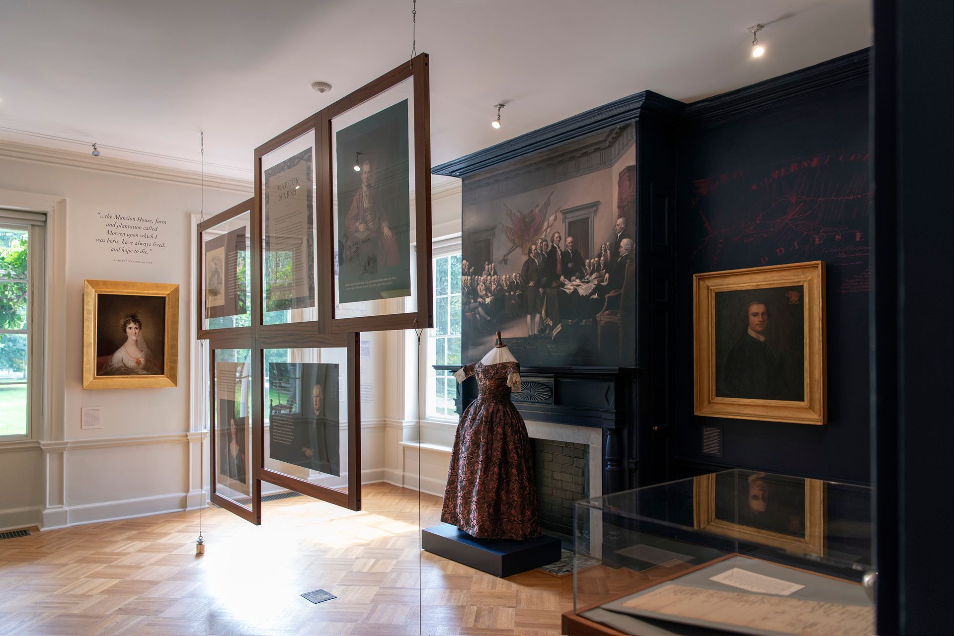 Art gallery room with framed portraits, an ornate dress on a pedestal, and a dark blue wall.