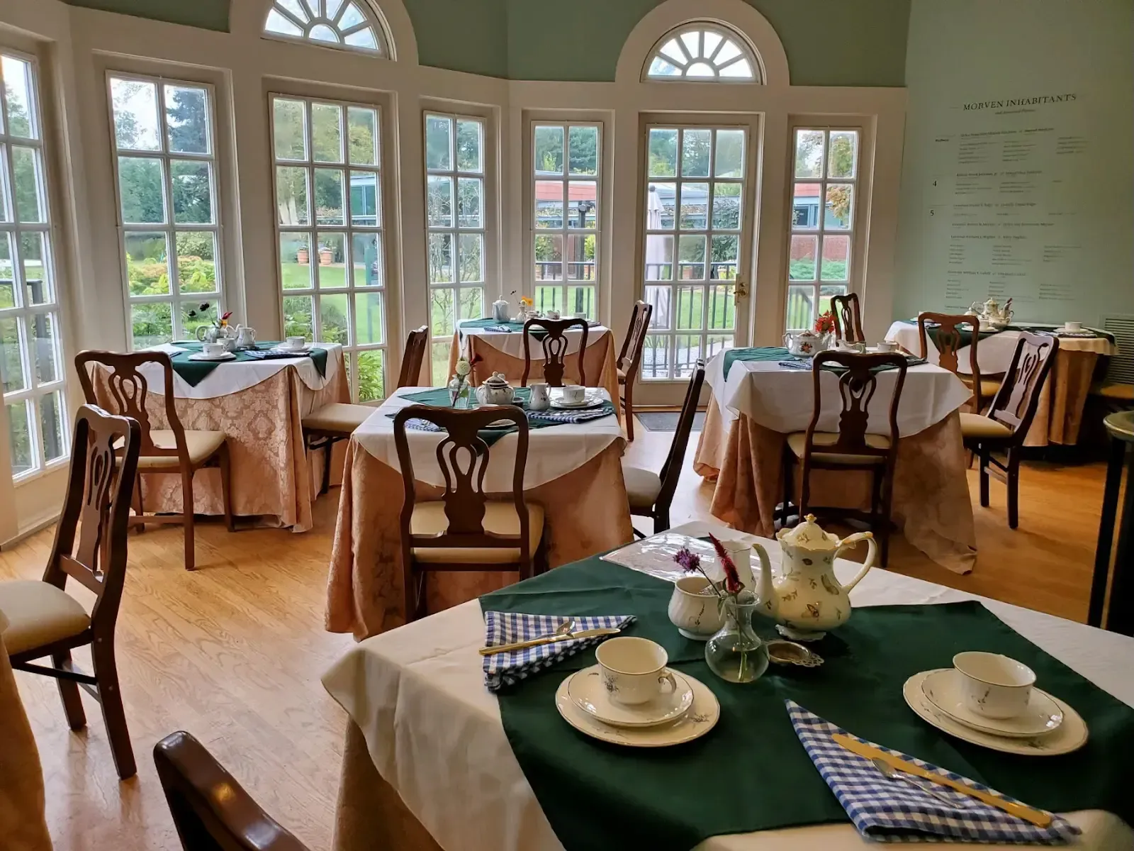 Tea setting on a table, with cups, teapot, and napkins. A window and chairs are in the background.