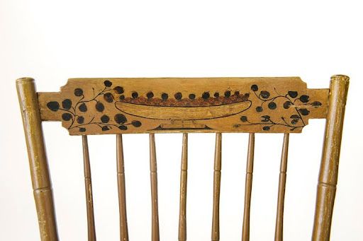 Close-up of a wooden chair back with black painted floral designs and a boat-like shape at the top.