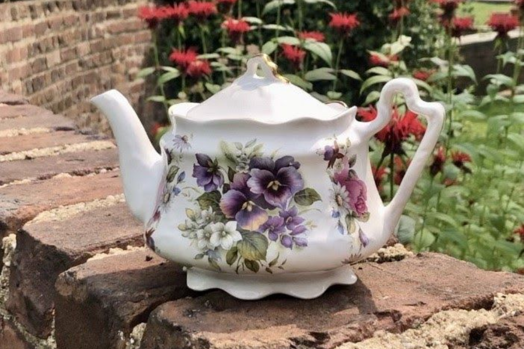 Tea setting on a table, with cups, teapot, and napkins. A window and chairs are in the background.