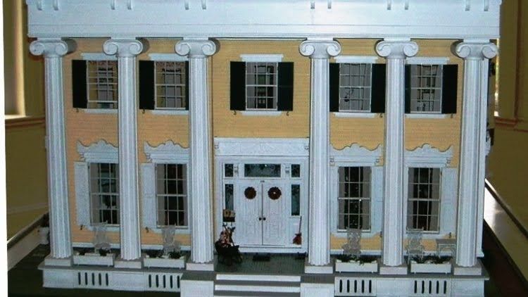 Dollhouse with yellow siding, white columns, black shutters, and double front doors.