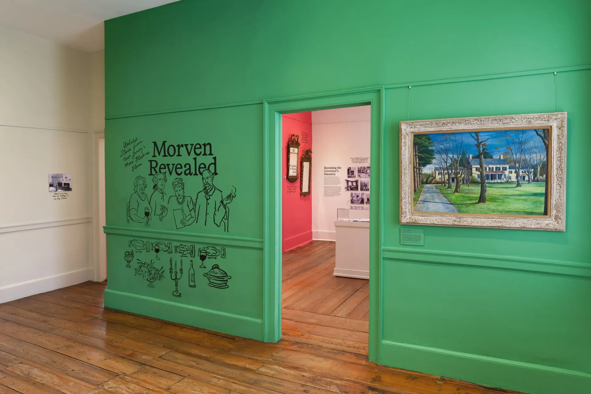 Museum gallery with green walls, doorway to pink room, artwork on wall, and wooden floor.