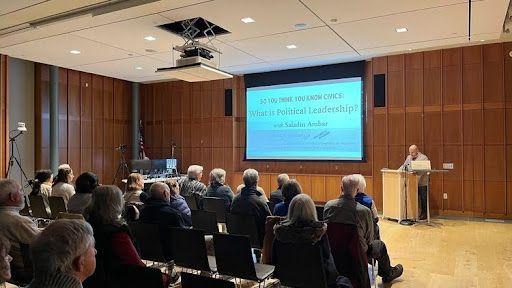 A man giving a presentation to an audience in a wood-paneled room.