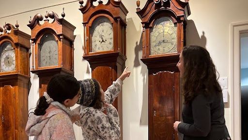 Three people examining antique grandfather clocks in a museum.