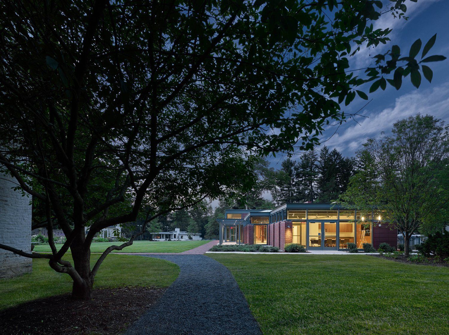 Modern house with large windows, pathway, and lush green lawn at dusk.
