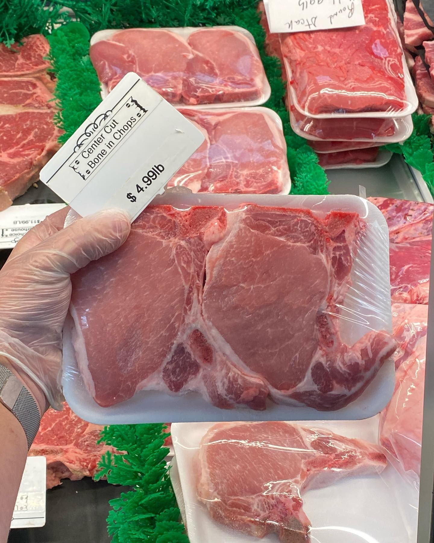 Person holding a package of raw pork chops in a butcher shop display.