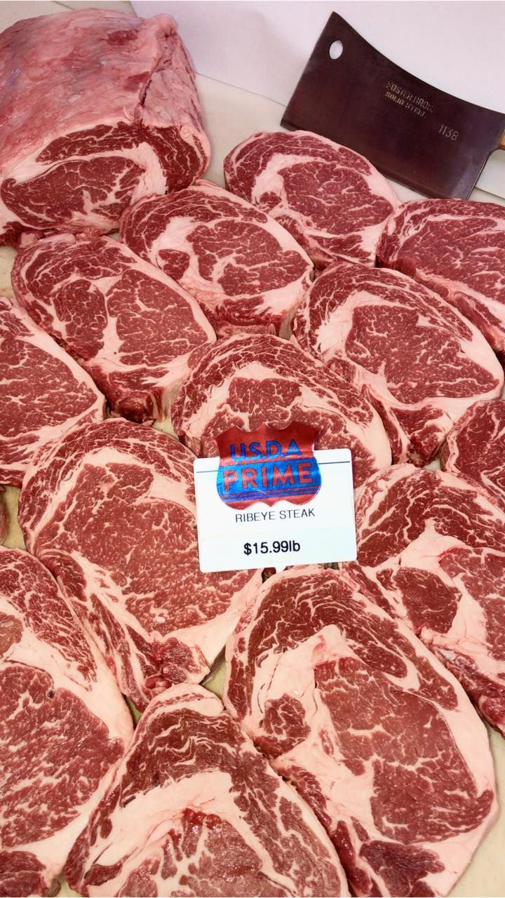 Raw ribeye steaks and a larger cut on display in a butcher shop. A cleaver rests nearby.