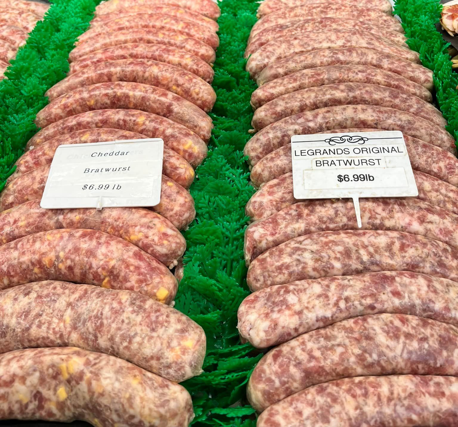 Rows of uncooked sausages on display in a butcher shop, with price tags.