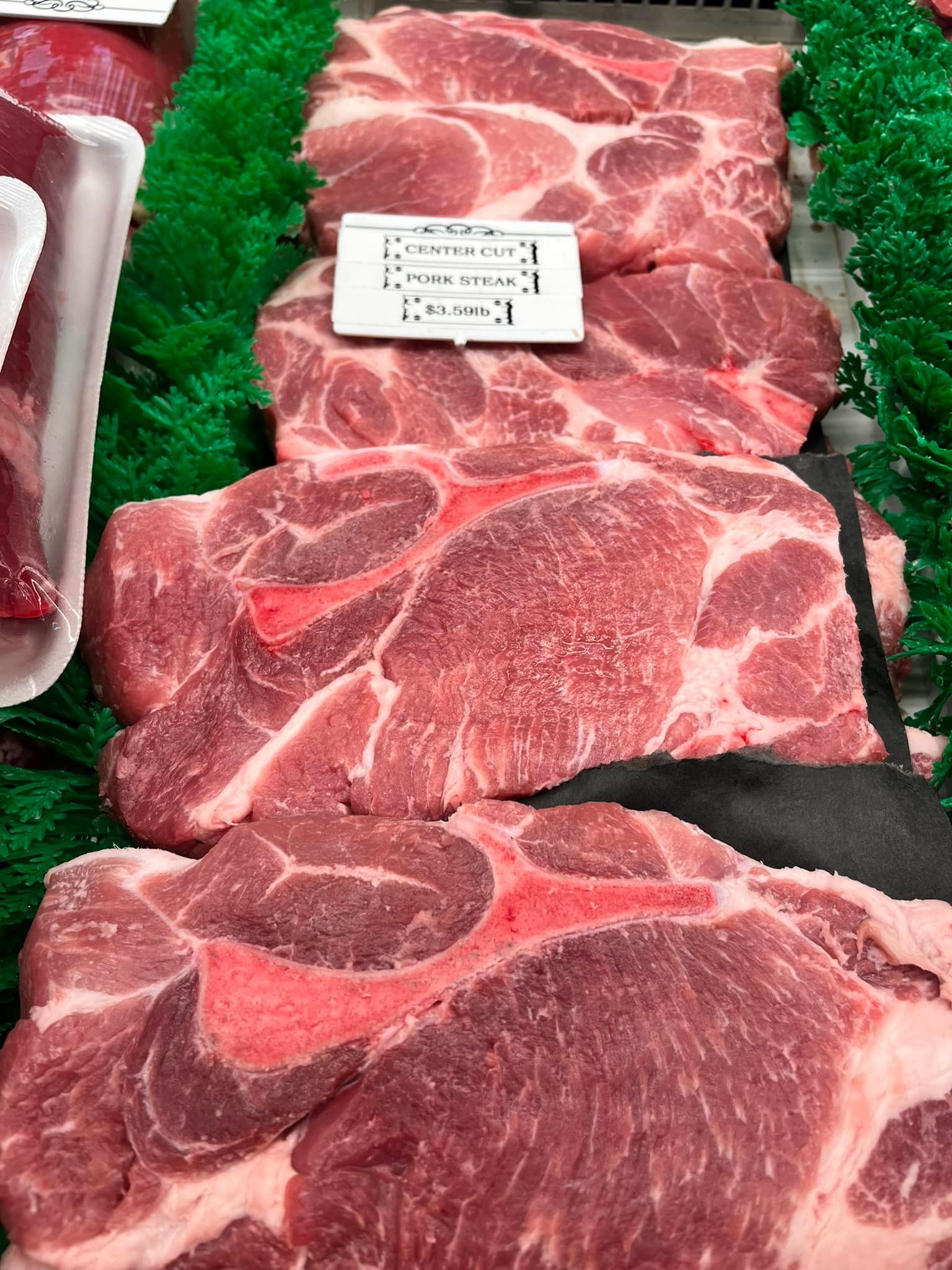 Raw pork shoulder cuts arranged in a butcher shop display, with a price tag.