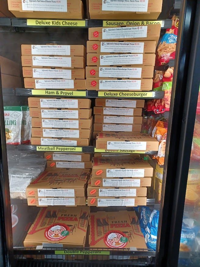 A refrigerated display case with stacks of pizza boxes, labeled with varieties.