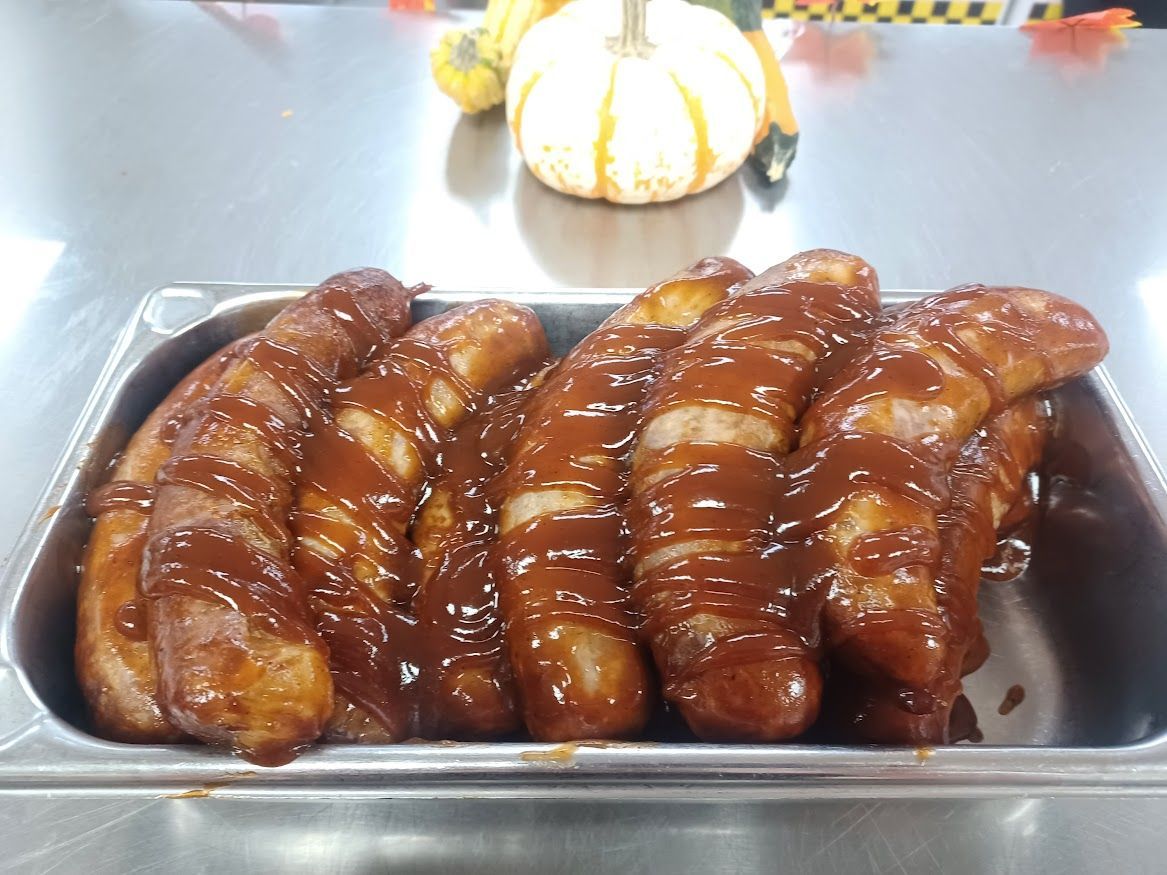 Sausage links in a stainless steel tray, glazed with barbecue sauce. Pumpkins in the background.