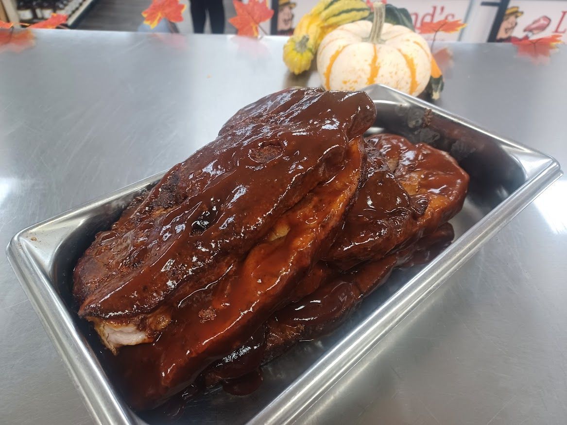 Barbecue ribs in a metal tray, covered in dark sauce, with pumpkins in the background.