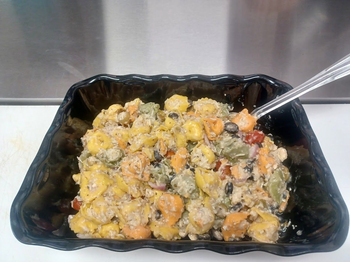Pasta salad in a black dish; includes corn, black beans, and colorful peppers. A fork is inserted.