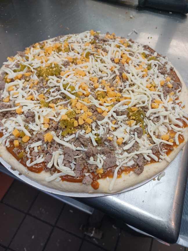 Pizza with meat, cheese, and peppers on a metal surface.