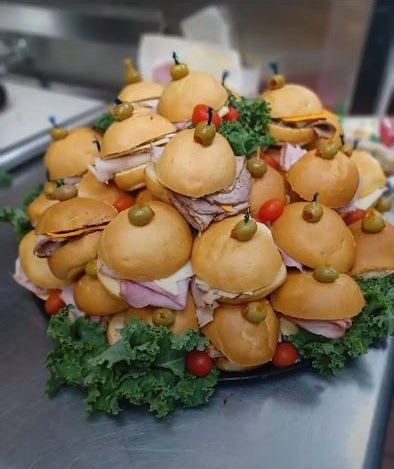 A platter of mini sandwiches, garnished with olives, tomatoes, and lettuce.
