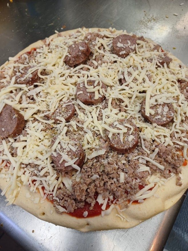 Pizza with sausage and ground meat, covered in cheese, on a metal surface.