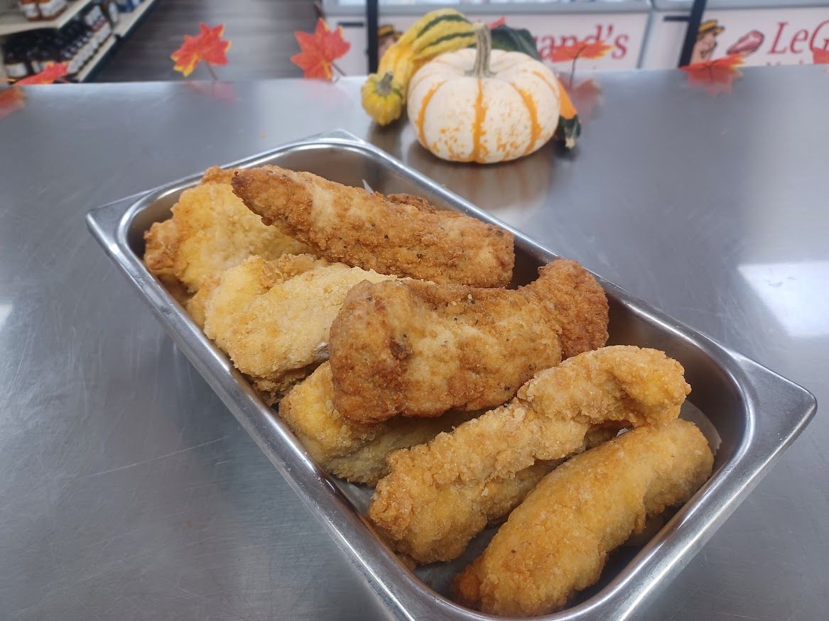 Fried chicken tenders in a metal tray on a counter, with a pumpkin and leaves in the background.