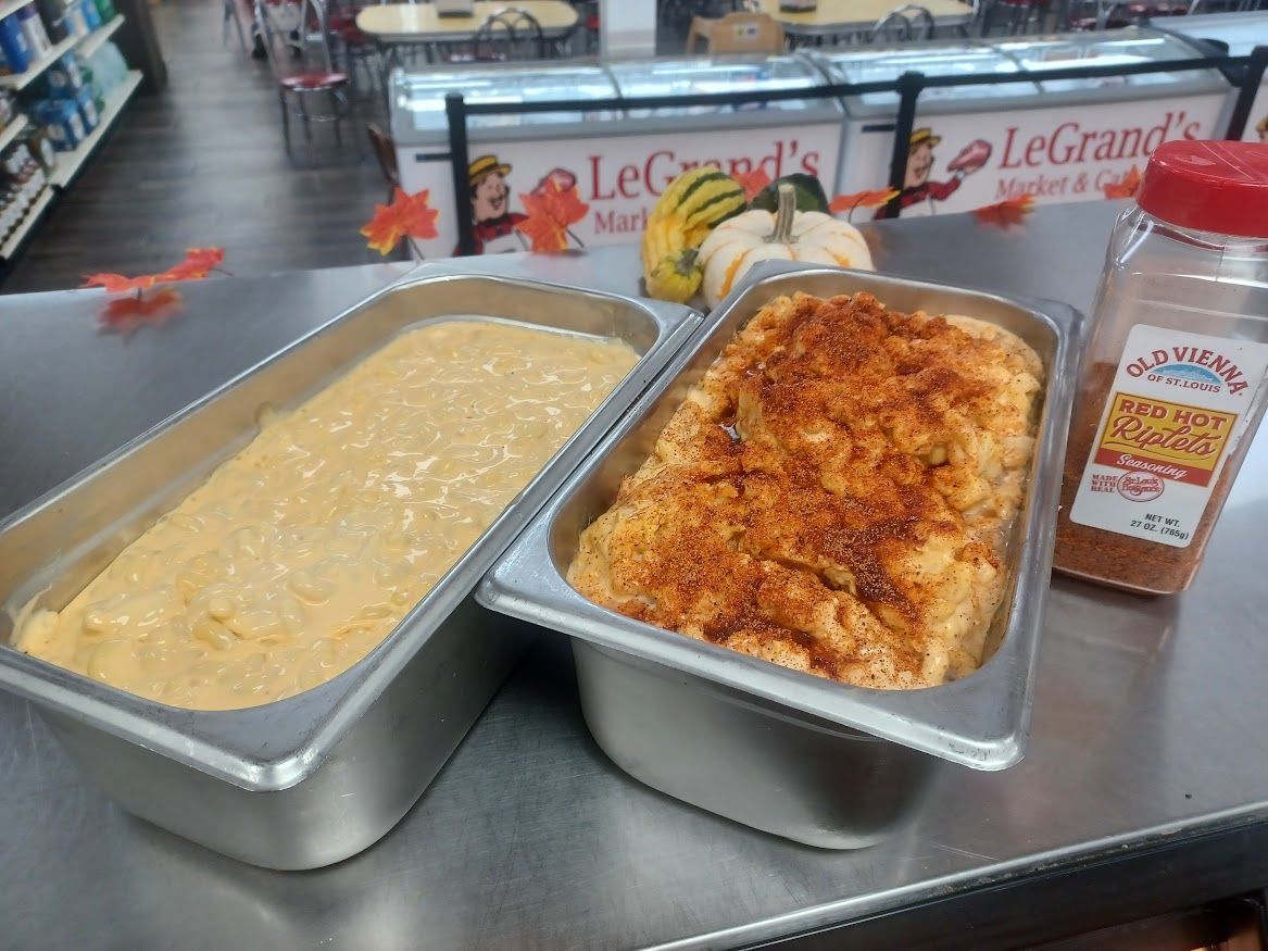 Two rectangular pans of prepared food, one plain, one with a reddish topping, sit on a counter in a store.
