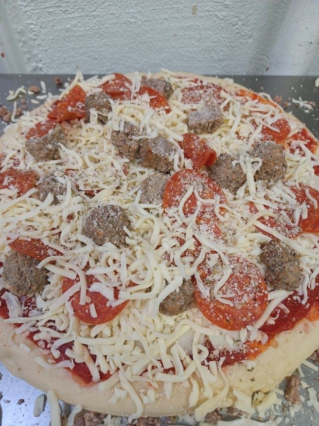 Pizza topped with sauce, cheese, pepperoni, and sausage, ready to be baked.